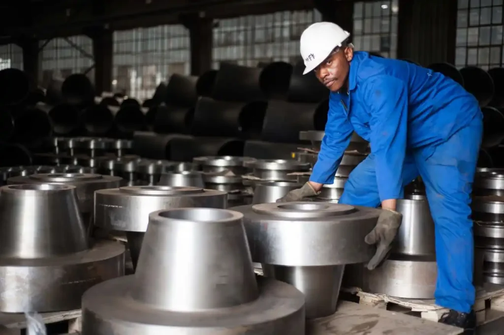 Pipechem worker wearing safety gear inspecting heavy forged steel weld neck pipe flanges in a Pipechem warehouse